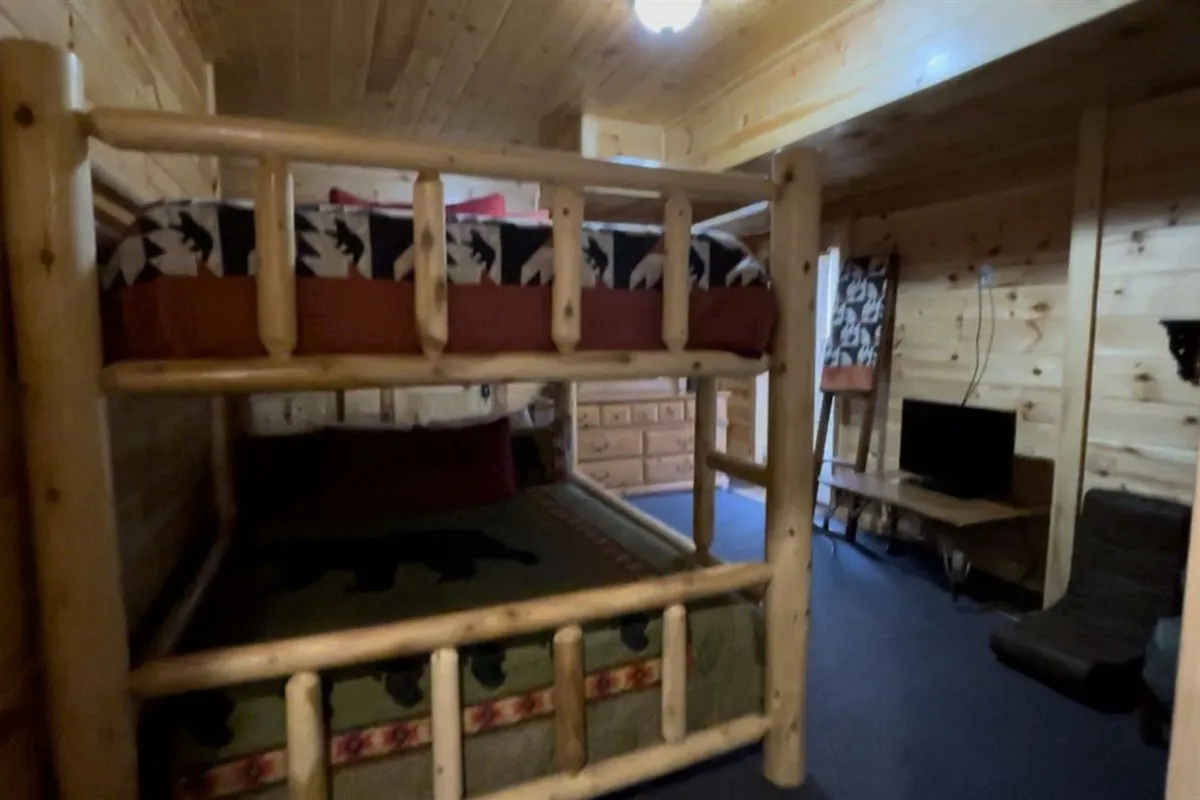 A cozy bunk room with a sturdy bunk bed, woven blanket, wooden furnishings, and a television. The space is welcoming and comfortable, ideal for kids or additional guests wishing to sleep, relax, or enjoy entertainment together.
