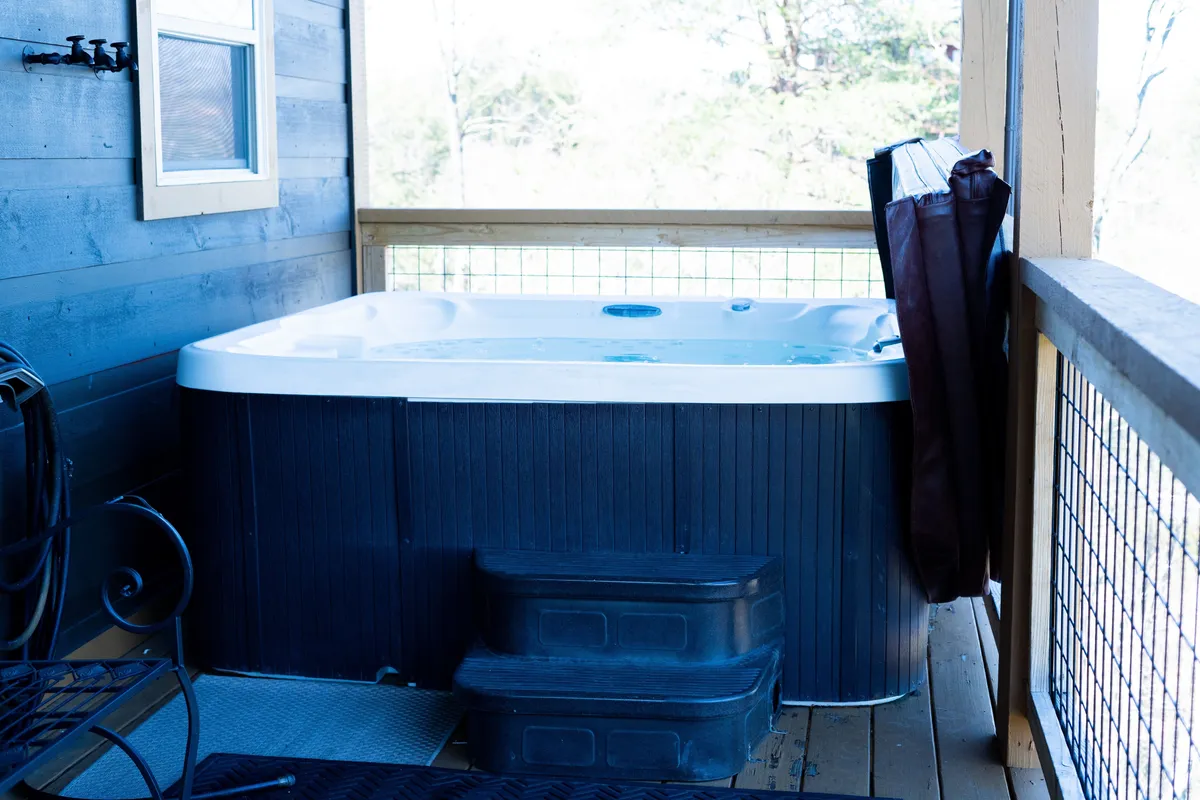 This interior image features a hot tub with bubbling water, stair steps, and a wooden railing. The setting is serene and private, inviting guests to unwind while enjoying views of the outdoors, possibly under the stars. The hot tub’s placement near a window or deck suggests easy access to fresh air and natural scenery.