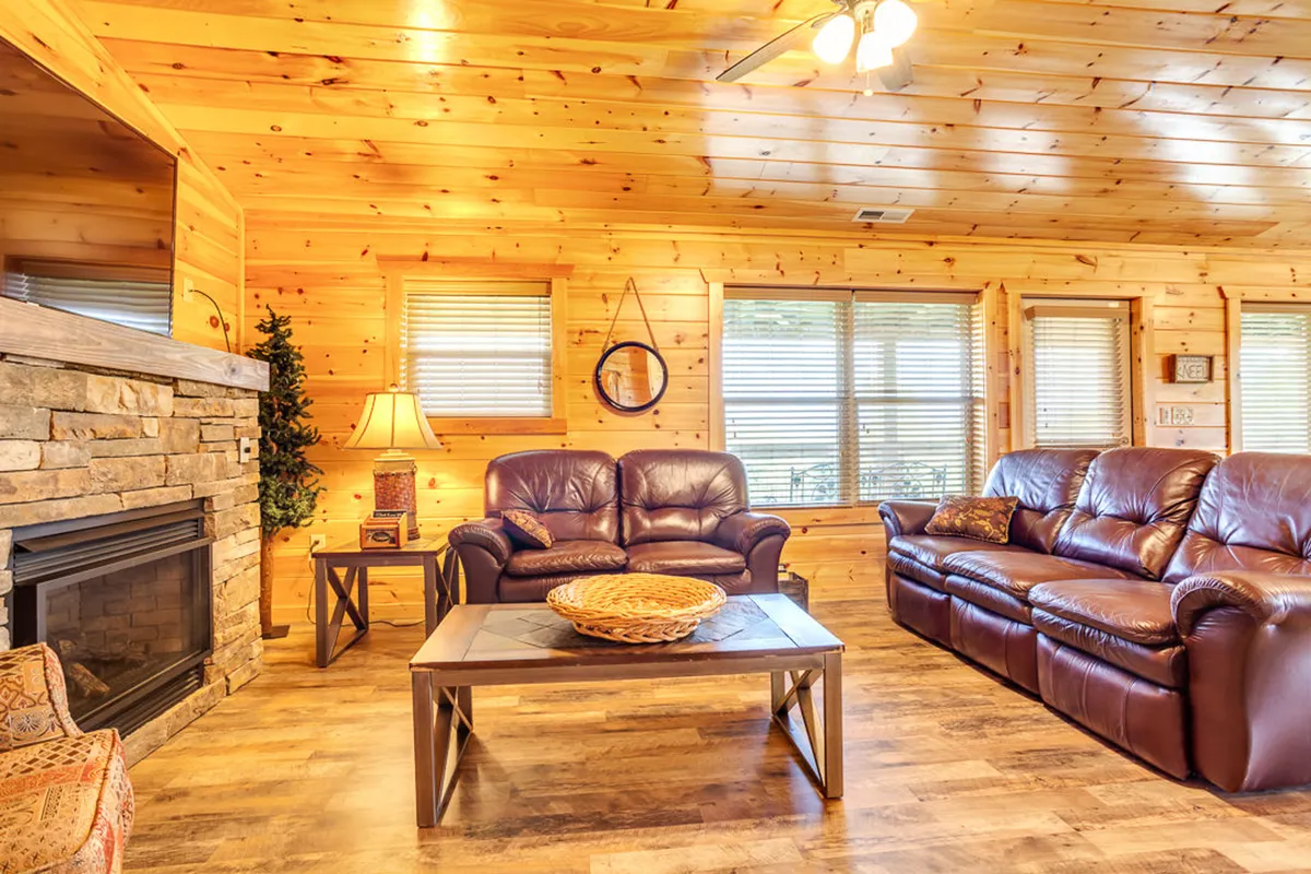 A cozy living area with a stone fireplace, leather sofas, a wooden coffee table, and a decorative lamp. The space is designed for relaxation and group gatherings, suggesting evenings spent socializing or enjoying fireside conversation.