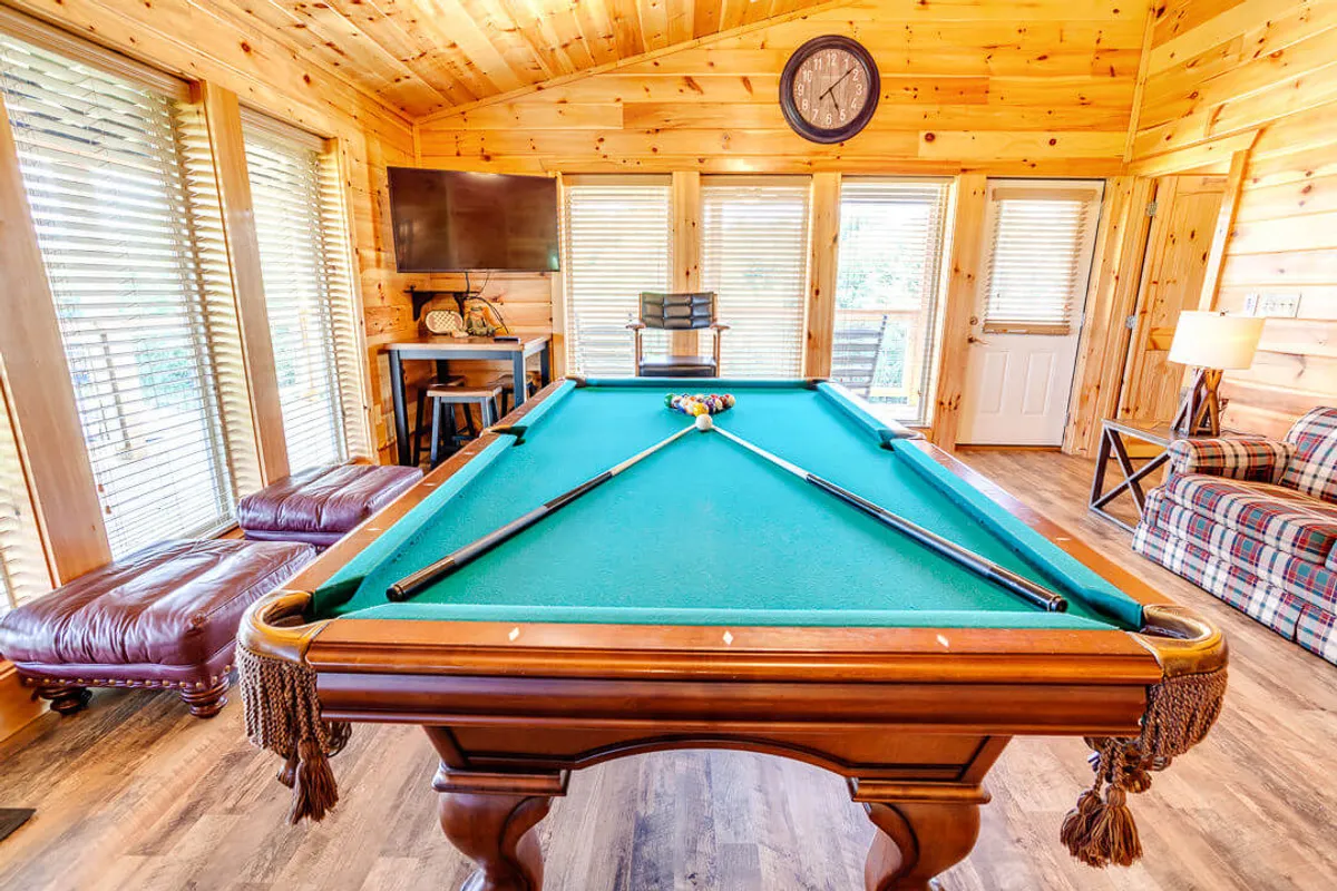 This image captures an inviting game and lounge area, complete with a pool table, leather chairs, wooden walls, and a television. The mood is lively yet relaxed, suggesting a space designed for fun, friendly competition, and casual socializing for guests of all ages.