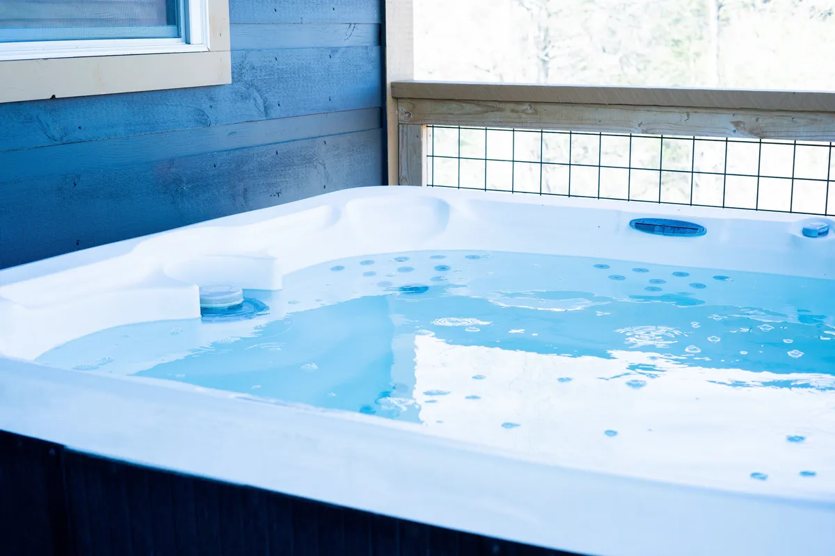A bubbling hot tub set against a wooden railing, suggesting an outdoor deck or patio with tranquil nature views. The scene conveys a relaxing spot perfect for unwinding after a day of mountain adventures, with the potential for stargazing or sunset watching.