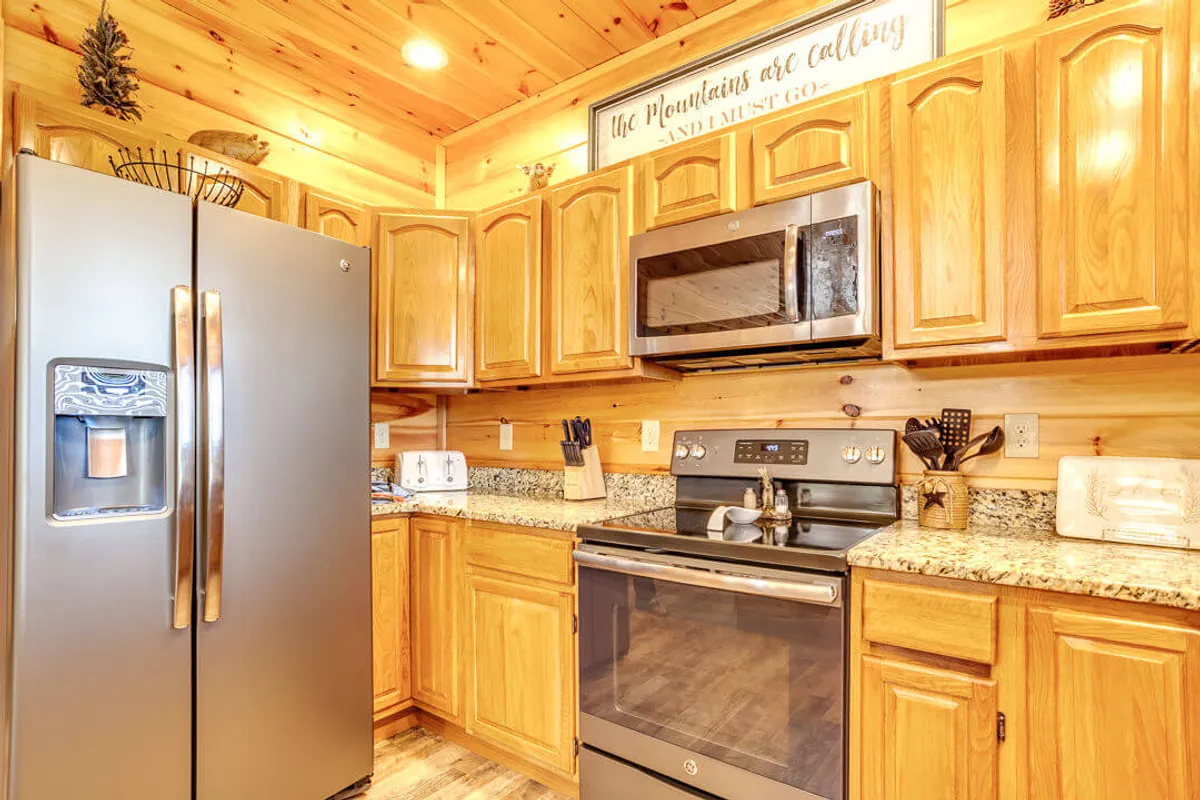 This image showcases a stylish and well-equipped kitchen featuring stainless steel appliances, granite countertops, warm wooden cabinetry, and a decorative sign. The central island and open layout invite gatherings and collaborative meal prep.